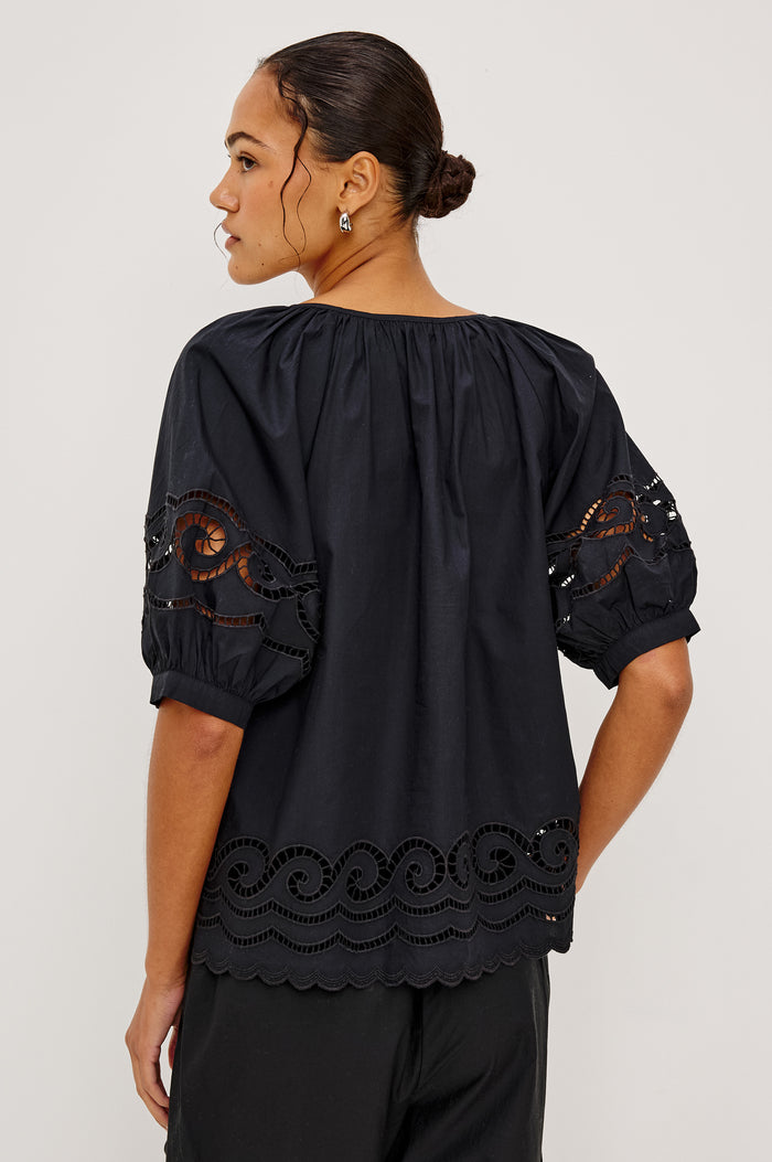 Catalene Peasant Blouse in Poplin With Self-Tie V-Neckline, Sheer Embroidered Detailing, Loose Fit, and Short Puff Sleeves in Black Colorway - Upper Body Back View Featured on Model