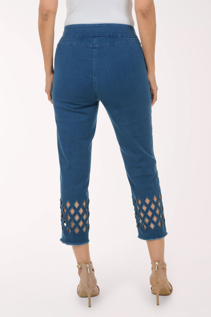 A model wearing blue cropped jeans with diamond-shaped cutout details near the hem, paired with a white top and beige strappy high-heeled sandals, against a plain white studio background.