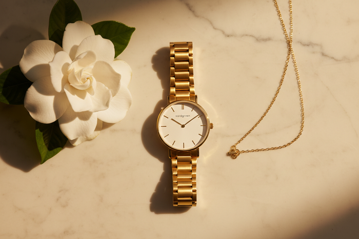 Nordgreen Native 28mm Gold 5-Link watch flat lay on ivory marble with gardenia
