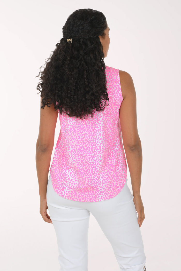 A woman modeling a sleeveless pink top with a white abstract pattern and a split neckline, paired with white pants, against a plain white background.