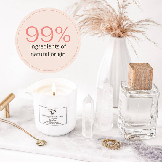 Taiga Massage Candle | Yon-Ka Paris lit on a marble surface surrounded by clear quartz crystals and a glass bottle with a wooden cap, promoting wellness and natural skincare with 99% ingredients of natural origin.