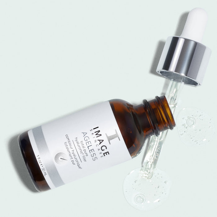 Brown glass dropper bottle lying down with clear serum and a dropper, labeled AGELESS total pure hyaluronic 6 filler | IMAGE Skincare on a light background, representing skincare product from Live Love Spa.