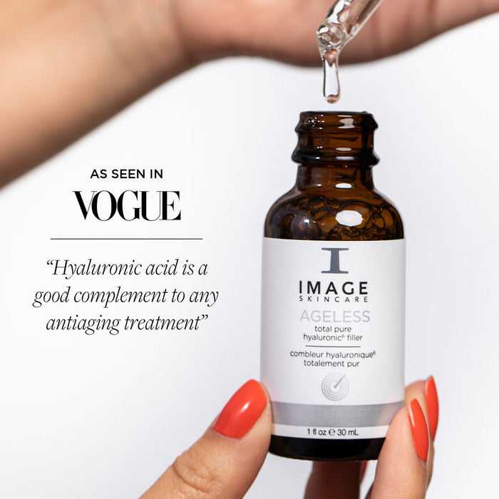 Hand holding a brown glass bottle with a dropper releasing serum, featuring AGELESS total pure hyaluronic 6 filler | IMAGE Skincare with a quote about hyaluronic acid and antiaging from Vogue in the background.