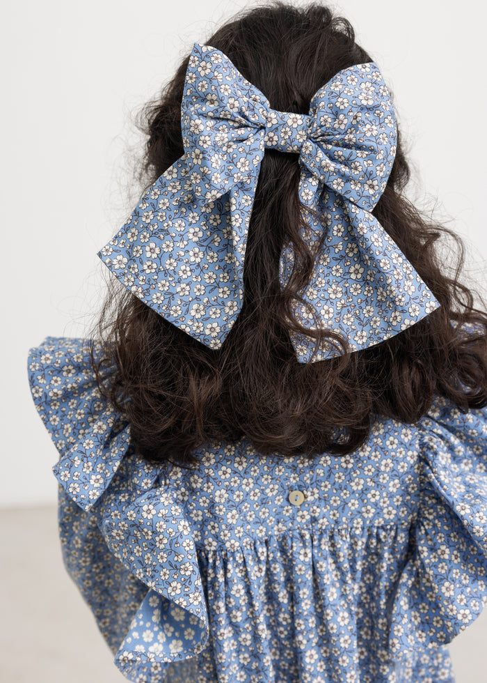 Hair clip with a large blue bow and small white flowers, placed in the hair