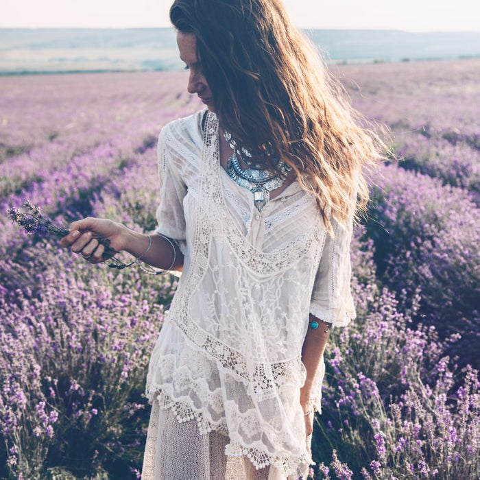 Woman in a white lace dress holding lavender in a purple flower field, evoking calm and natural beauty aligned with Antioxidant Repair | Privai skincare and wellness.