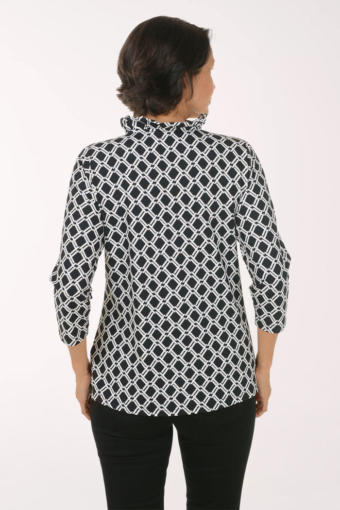 A woman modeling a black and white geometric patterned blouse with three-quarter sleeves and a V-neck, paired with black pants, against a plain white studio background.