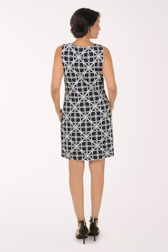 A woman modeling a sleeveless knee-length shift dress with a black and white geometric interlocking circle pattern, paired with black strappy high-heeled sandals against a plain white studio background.