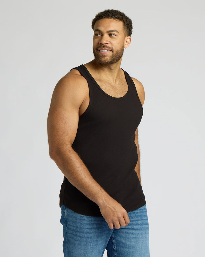Man wearing a black tank top and blue jeans on a light gray background