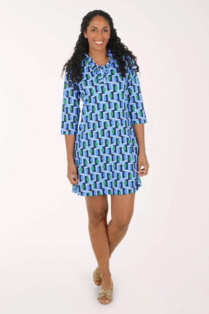 A woman modeling a short-sleeve button-up shirt dress with a blue, green, and white geometric pattern, standing against a plain white studio background.