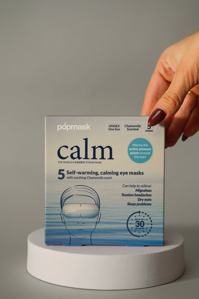 Box of Calm Self Warming Pressure Point Eye Mask - Single | Popmask with soothing chamomile scent being held, promoting relief for migraines, tension headaches, dry eyes, and sleep problems.