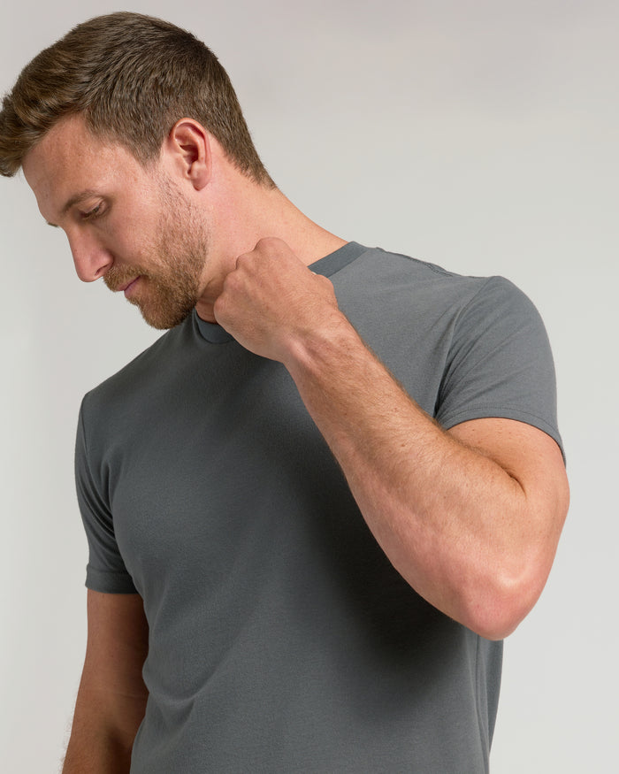 Man wearing Carbon Classic Crew Neck, adjusting neckline, against light background.