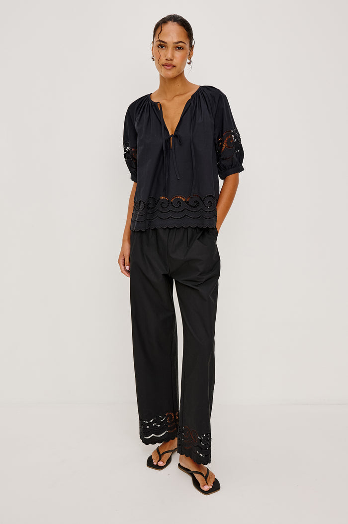 Catalene Peasant Blouse in Poplin With Self-Tie V-Neckline, Sheer Embroidered Detailing, Loose Fit, and Short Puff Sleeves in Black Colorway - Full Body Front View Featured on Model