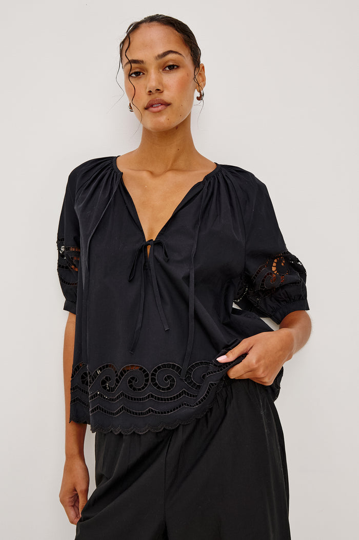 Catalene Peasant Blouse in Poplin With Self-Tie V-Neckline, Sheer Embroidered Detailing, Loose Fit, and Short Puff Sleeves in Black Colorway - Upper Body Front View Featured on Model