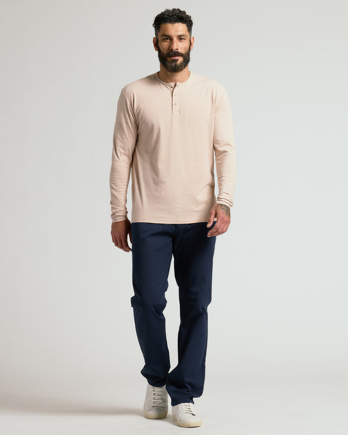Man wearing a beige long-sleeve shirt and navy pants on a light gray background