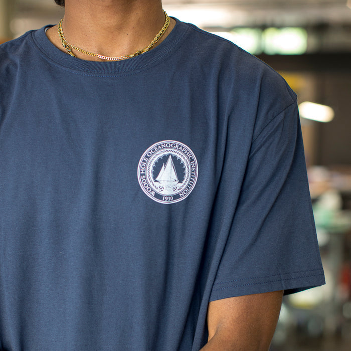 Close up of the WHOI Classic Seal in white on a navy t-shirt.