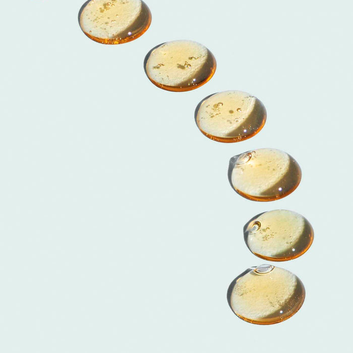 Close-up of clear golden gel droplets on a light surface, representing the texture of CLEAR CELL clarifying acne spot treatment | IMAGE Skincare for targeted skincare use.
