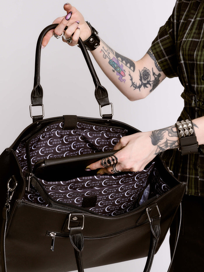 Person holding a black handbag with a patterned interior, wearing tattoos and rings.