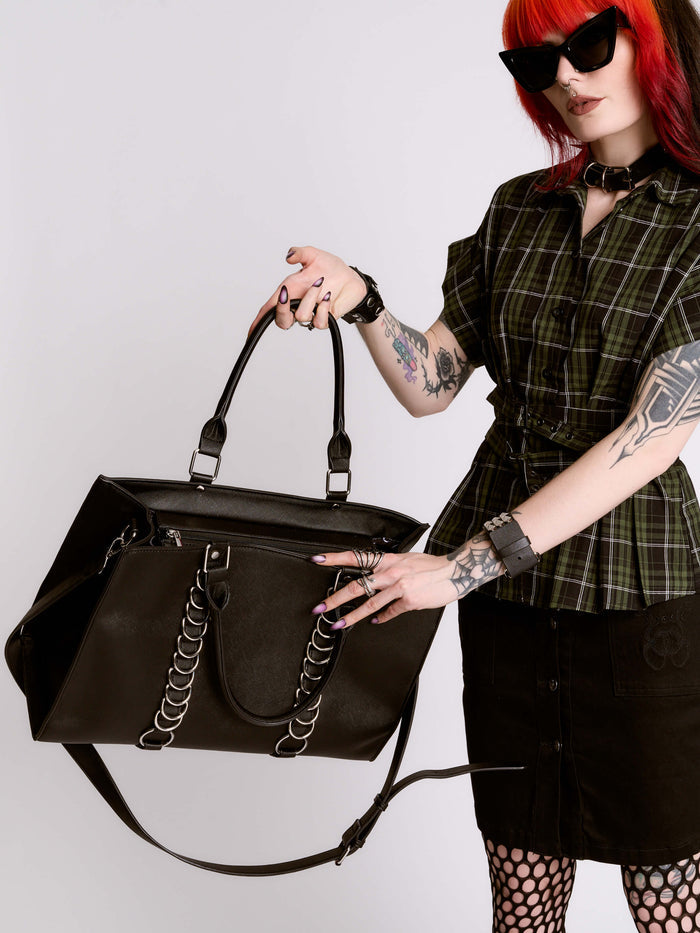 Person holding a black handbag with a plain background