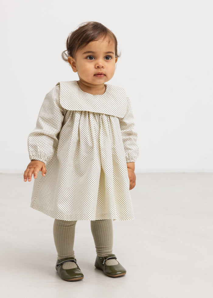 Baby with a polka dot dress with loose fit and long sleeves, plus gray socks.