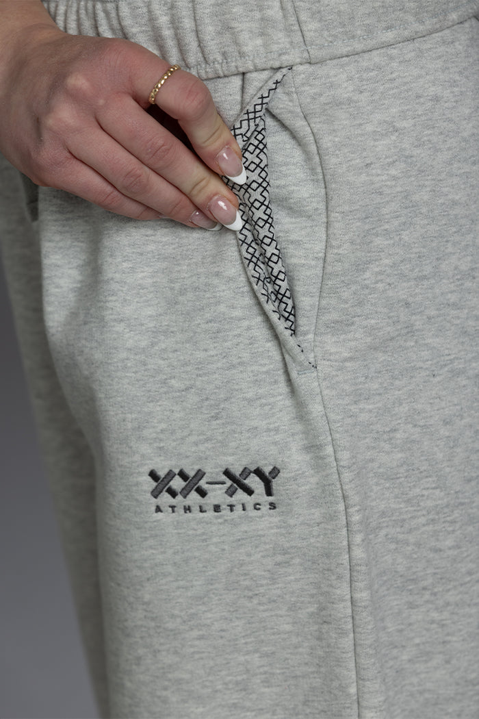 Gray sweatpants with a brand logo on the pocket, held by a hand. || Light Heather Gray