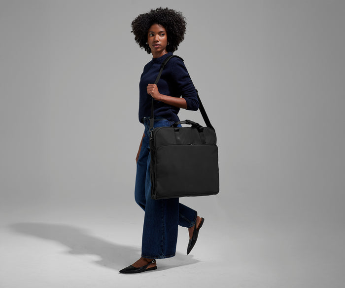 A female model carrying the Garment Bag in Jet Black over her shoulder using the adjustable, removable shoulder strap
//
Model is 5'9"
