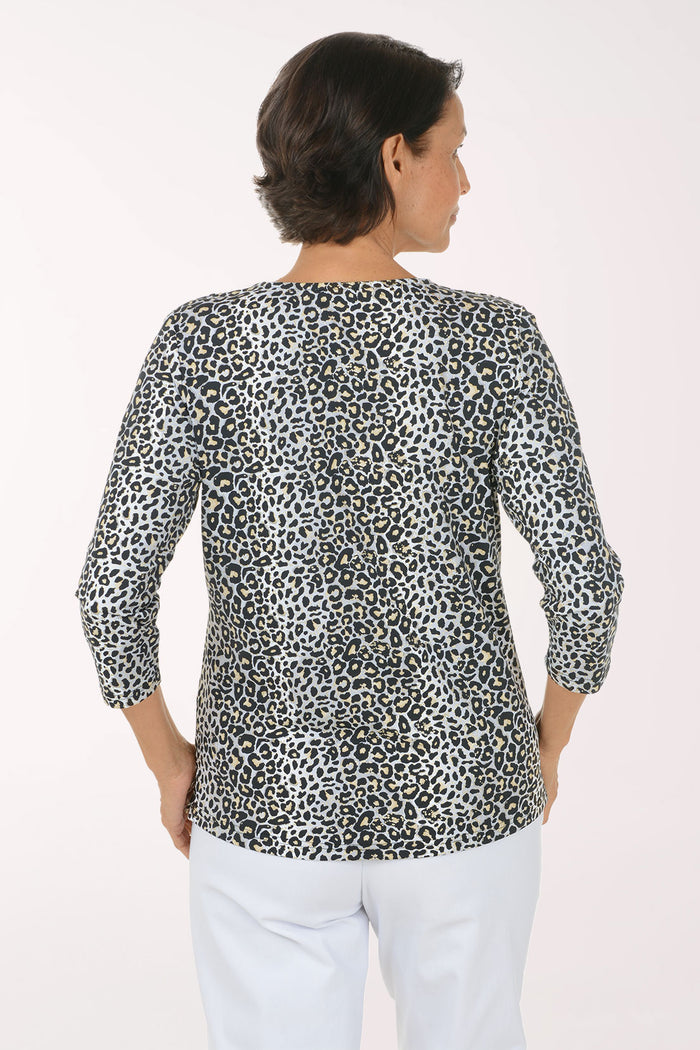 A woman modeling a black and white leopard print long-sleeve top with a V-neck, paired with white pants, against a plain light background.