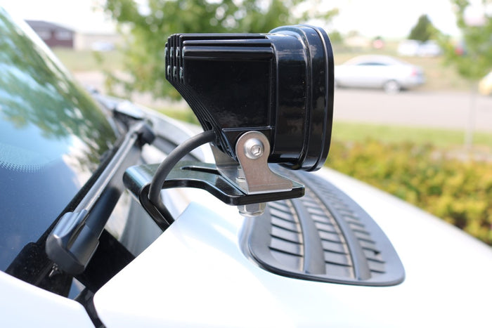 Close-up of a Hoodline Light Pod Mount for Sprinter (2019+), installed on the car's hood hinge, designed for LED pod lights.