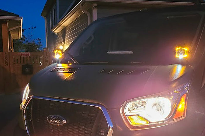 Hoodline light pod mount for Transit vans (2013+), shown installed on a vehicle with lights on. Mounts to factory fender bolts, lights not included.