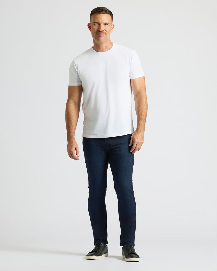 Man wearing Indigo Wash Slim Comfort Stretch Jeans, white T-shirt, black sneakers.