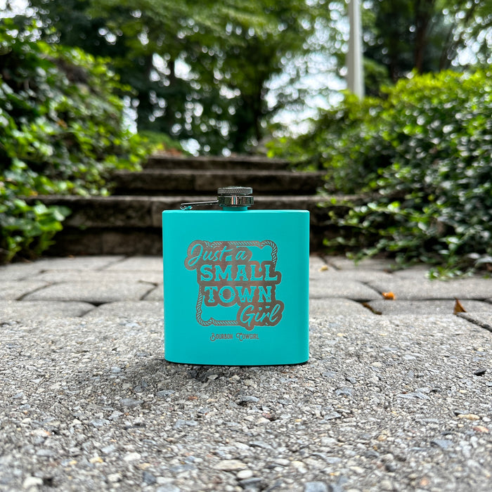 Teal flask with Just a Small Town Girl on a stone surface.
