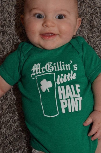 A smiling baby wearing a green onesie with the text 'McGillin's Little Half Pint' and a shamrock symbol on it.