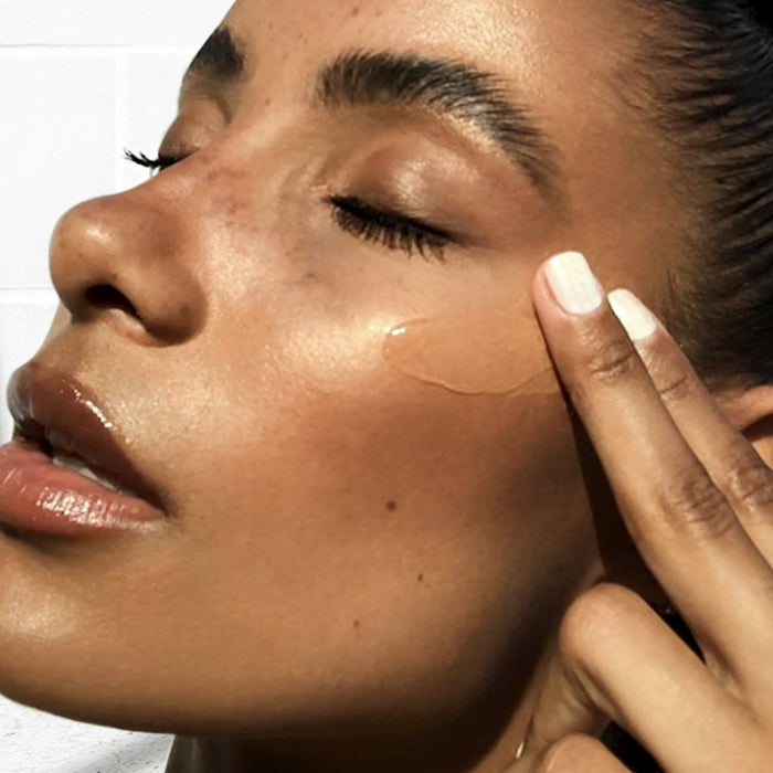 Close-up of a woman with glowing skin applying NuFACE FIX® Serum | NuFACE under her eye, demonstrating skincare and wellness beauty routine.