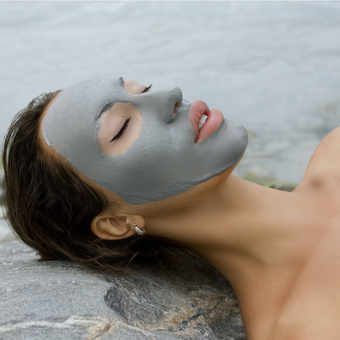 Woman relaxing outdoors with eyes closed and face covered in gray clay masque, showcasing skincare treatment using Phyto Clay Masque | Privai for a soothing wellness experience.