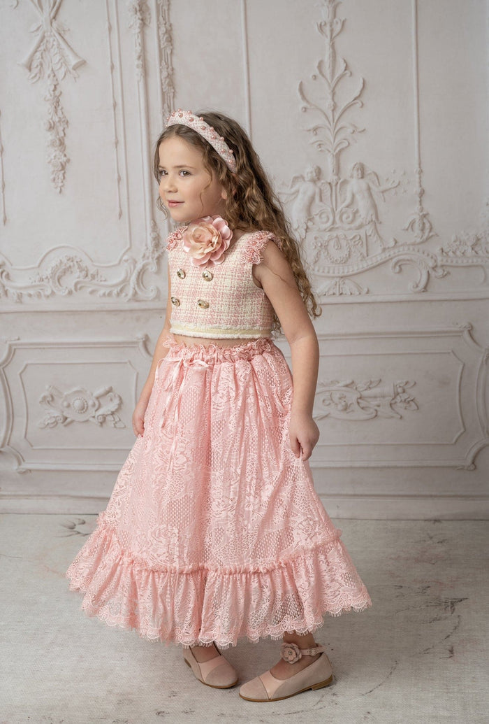 Full outfit view of child wearing pink flower neck tie with a blush skirt and top, styled for an elegant occasion