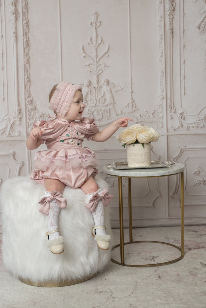 Baby wearing a pink ballerina hair sash with pleated fabric and jewel details, styled with a matching pink ballerina outfit in a classic studio setting