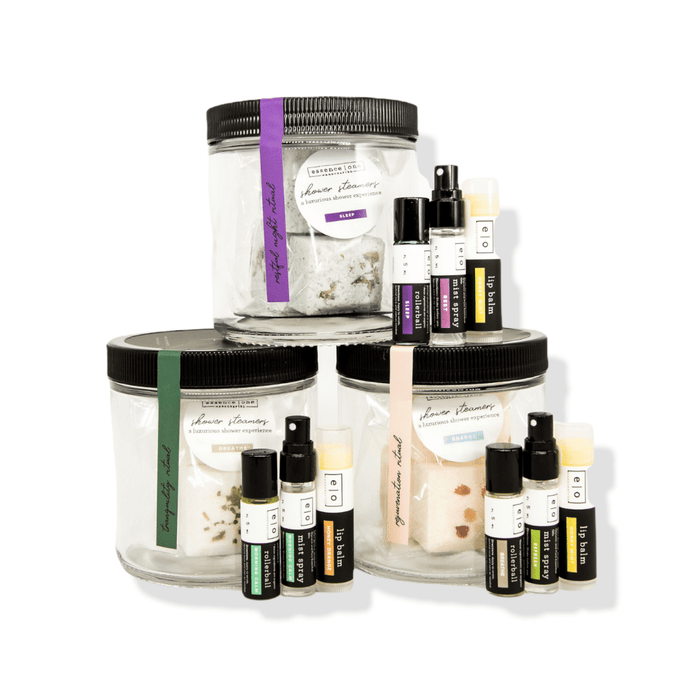 Three clear jars with black lids containing various natural shower steamers and small wellness supplement bottles, arranged together as the Ritual Kit | Essence One.