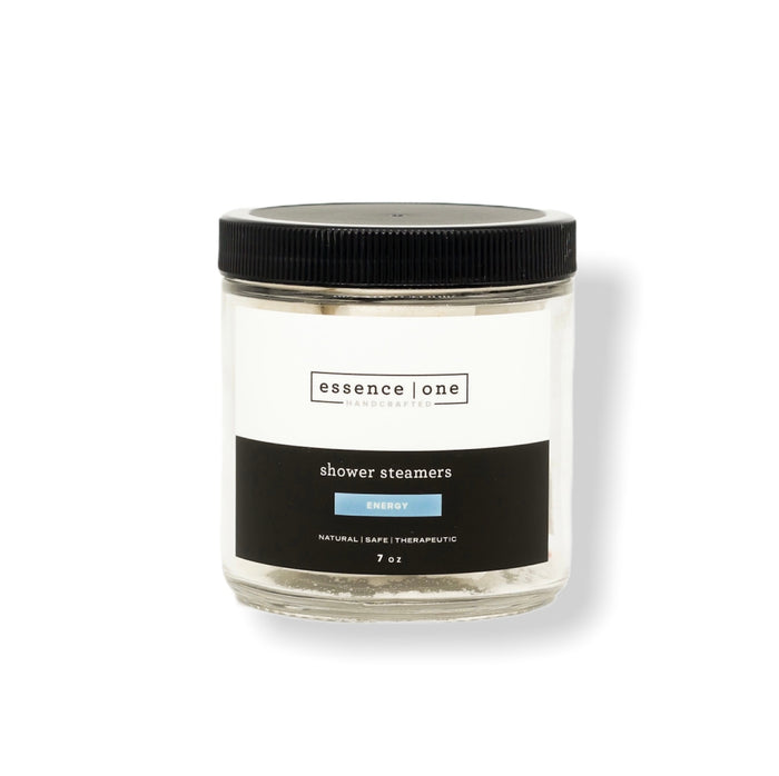 Clear glass jar with black lid containing Shower Steamer | Essence One, labeled as energy with a natural, safe, and therapeutic formula for wellness and body care.