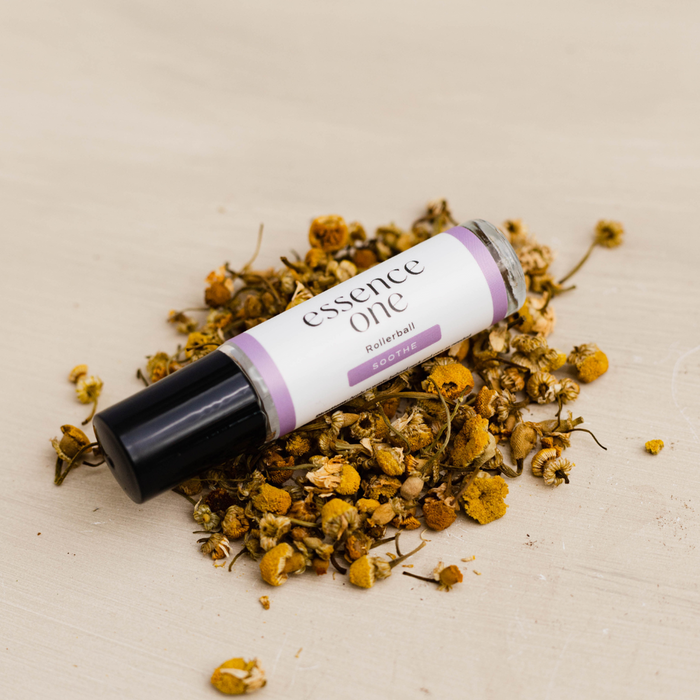Soothe Rollerball - Abdominal Support | Essence One on a light surface surrounded by dried chamomile flowers, highlighting a natural skincare and wellness body care product.
