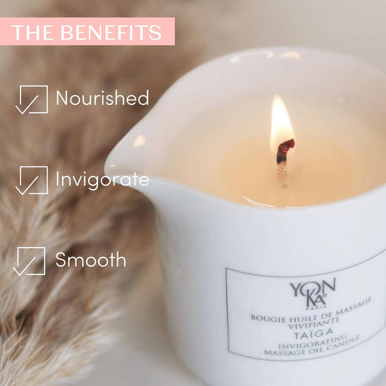 Close-up of a lit Taiga Massage Candle | Yon-Ka Paris in a white container surrounded by soft beige textures, highlighting benefits of nourished, invigorate, and smooth skin.