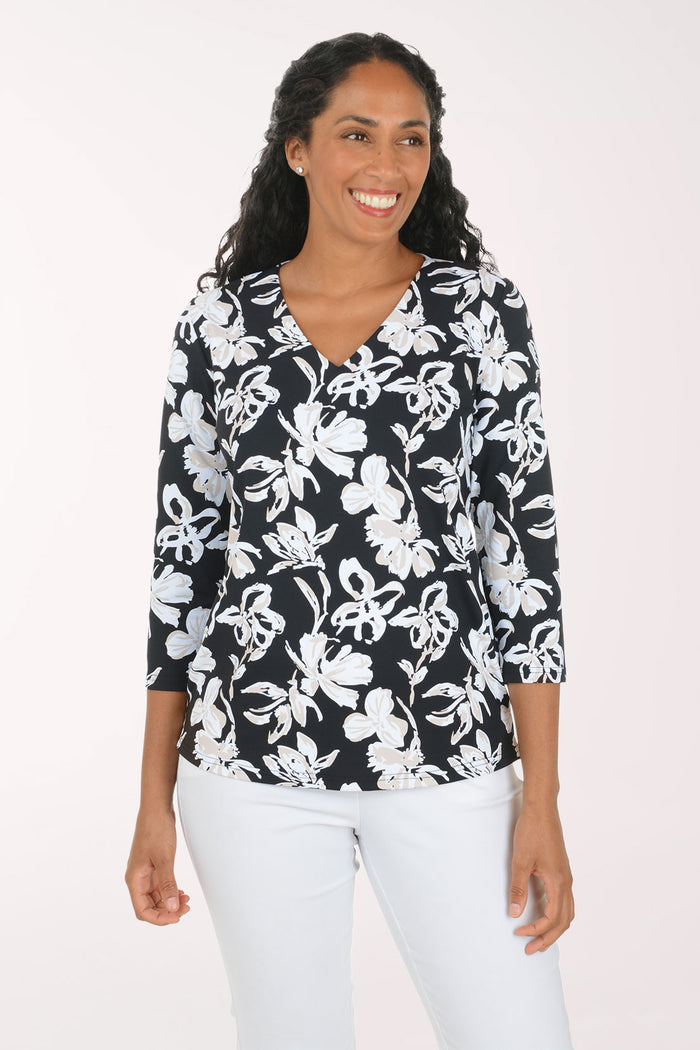 A woman modeling a black and white floral print top with three-quarter sleeves and white pants, standing against a plain light background.