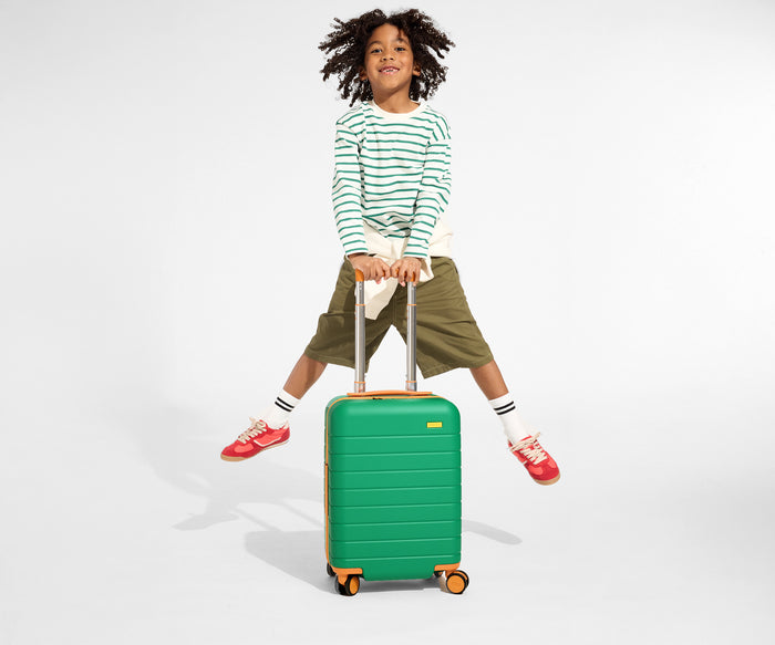 A child model holding the raised handle of The Kids Carry-On suitcase in Froggy Green and jumping in the air with a smile on their face
//
Daniel, age 8, with The Kids Carry-On in Froggy Green.