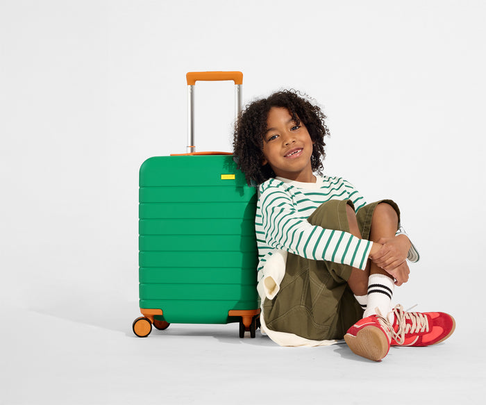 A child model sits on the floor and leans against The Kids Carry-On suitcase in Froggy Green
//
Daniel, age 8, with The Kids Carry-On in Froggy Green.