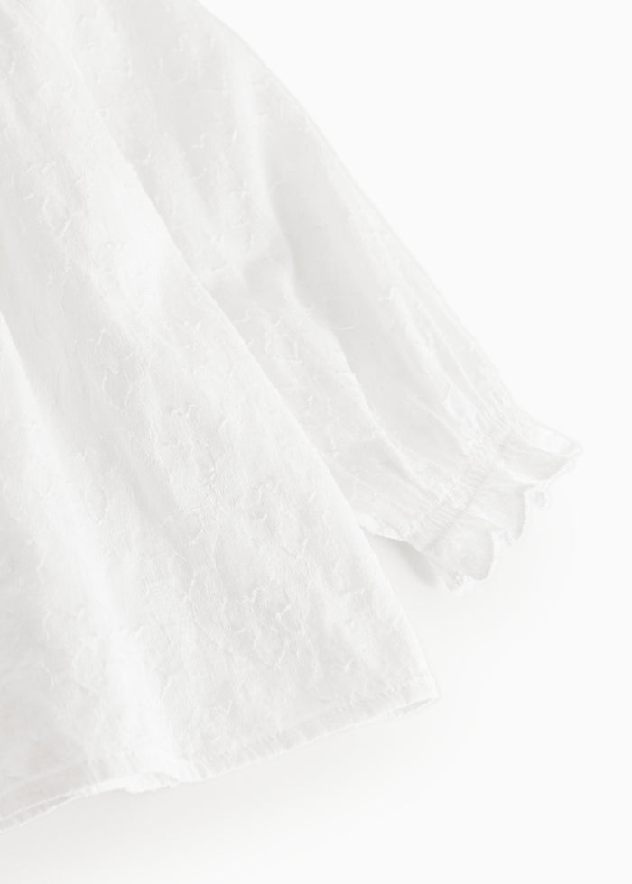 White baby blouse with a ribbed edge at the sleeves and lightly textured fabric.